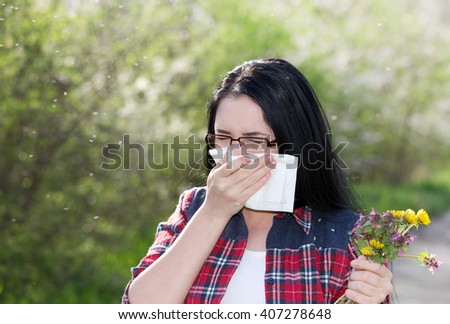 Young girl holding bouquet of wildflowers and blowing nose in tissue paper. Allergies concept