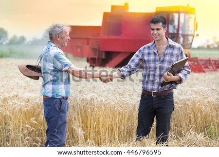 Two farmers shaking hands on wheat field while combine harvesting behind