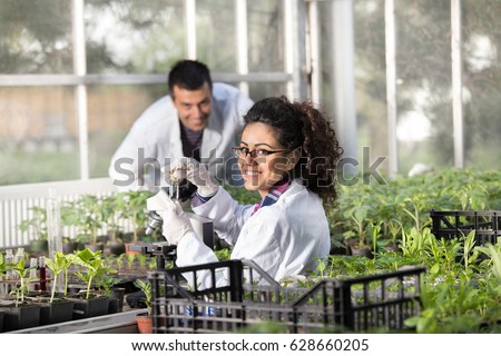 Two young smiling engineers working in greenhouse with sprouts. Plant protection and care concept