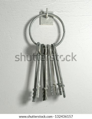 A set of old jail keys on a hoop hanging on a metal hook on a white wall