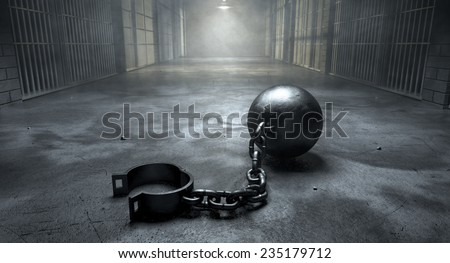 A vintage ball and chain with an open shackle on an old prison cell block floor lit by overhead lights