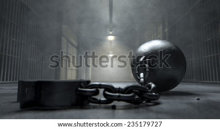 A vintage ball and chain with an open shackle on an old prison cell block floor lit by overhead lights