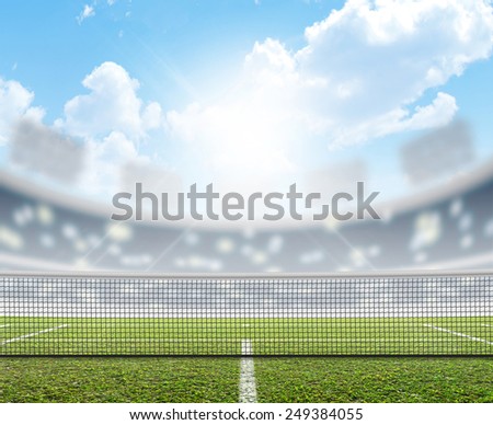A tennis court in an arena with a marked green lawn surface in the daytime under a blue sky