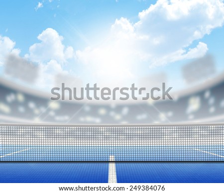 A tennis court in an arena with a marked hard blue surface in the daytime under a blue sky