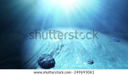 An underwater scene at the bottom of the ocean floor showing sand and emanating sunlight beaming through