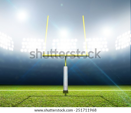 A football stadium with posts on a marked green grass pitch in the night time illuminated by an array of spotlights