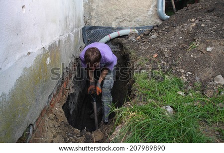 Man preparing hole in ground for Installation of new studded film as insulation against ground moisture