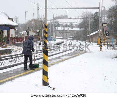 Woman with shovel clears snow from a platform on the  station