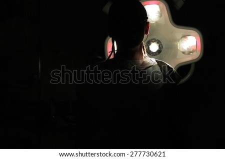 Silhouette of  male nurse ICU  with  dreadlocks on black background with operating lamp.
