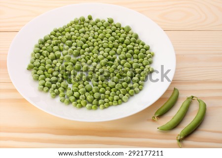 Green peas  in white plate  and pea pods  on wooden table,closeup