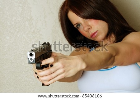 Close up image of young attractive female pointing gun at someone breaking and entering