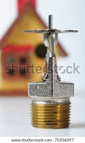 Close up image of fire sprinkler on white. Fire sprinklers are part of an integrated water piping system designed for life and fire safety.  Replica of house added to background.