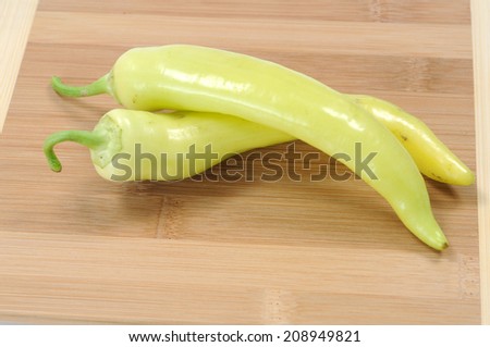 two banana peppers on wooden cutting board