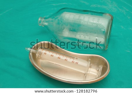 Glass syringe in  sterile basin and  glass bottle for tube feeding diet
