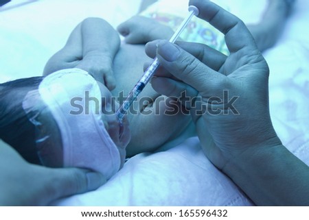 Doctor giving remedy to premature baby  under ultraviolet lamp in the incubator