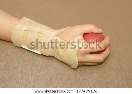 woman's hand with wrist support squeezing a soft ball for hand rehabilitation