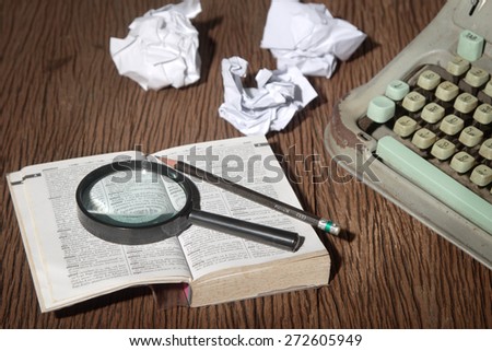 The thai-english dictionary consider under a magnifier on writer\'s desk with crumpled sheets around