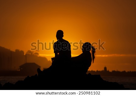 Silhouette of man and women against sunset over Gordons Bay in the Western Cape Province of South Africa