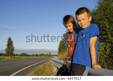 Boys sitting on a fence by the road