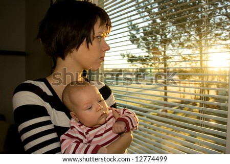 Young mother looking out from the window with her baby