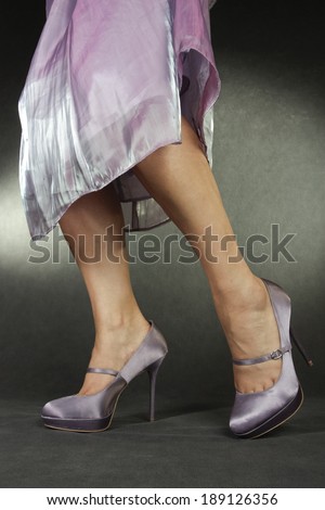 Woman wearing lilac satin dress and heels over grey background