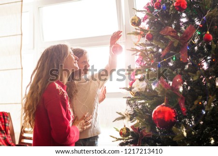 Mom and daughter decorate the Christmas tree. Happy family at home