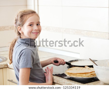 Child bakes pancakes in the kitchen. Girl cooking breakfast
