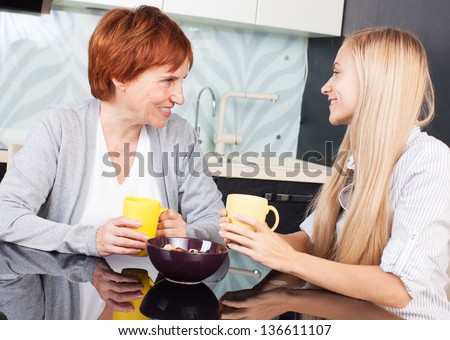 Happy adult woman with daughter on kitchen. Family at home talking and drinking tea