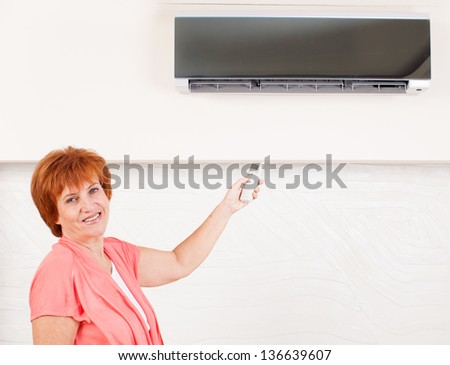 Woman holding a remote control air conditioner at home. Happy mature woman on sofa