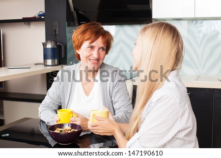 Happy adult woman with daughter on kitchen. Family at home talking and drinking tea
