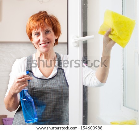 Mature woman cleaning window. Female washing window