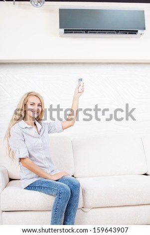 Female holding a remote control air conditioner at home. Happy young woman on sofa