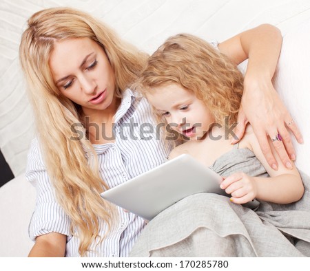 Family wiht tablet at sofa. Woman and baby with tablet computer. Mother and daughter at home on sofa