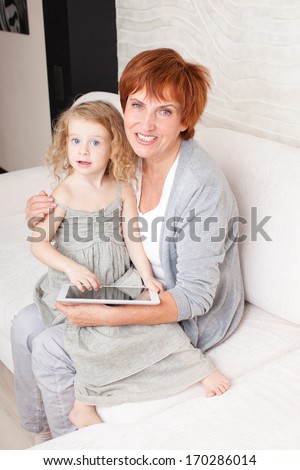 Family wiht tablet computer at sofa. Grandmother and little girl at home on sofa. Generation