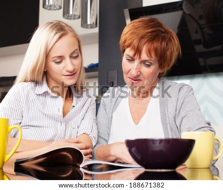 Mother and daughter read magazine at home. Happy women on the kitchen