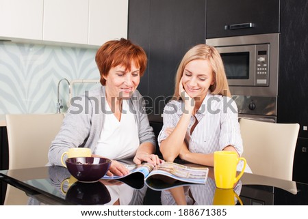 Mother and daughter read magazine at home. Happy women on the kitchen