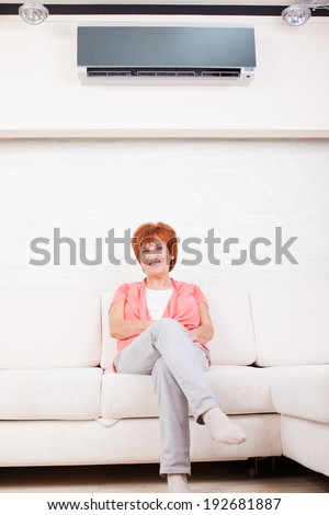 Woman under the air conditioner at home. Happy mature woman on sofa