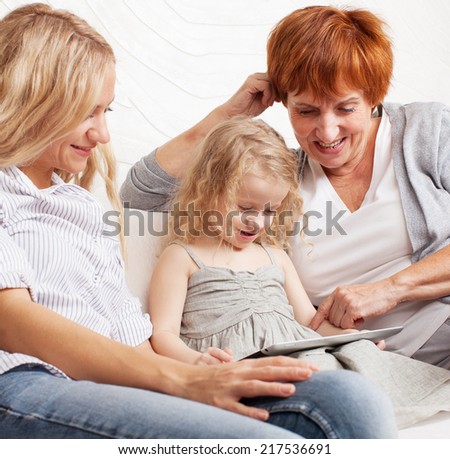 Family wiht tablet computer at sofa. Mother, grandmother and little girl at home on sofa. Generation