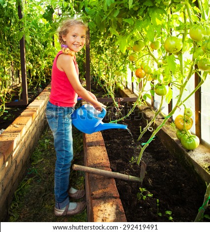 Child watering the garden. Girl helps to do the work in the greenhouse