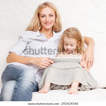 Family with tablet at sofa. Woman and baby with tablet computer. Mother and daughter at home on sofa