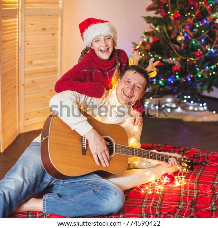 Child with a dad playing the guitar and singing near christmas tree. Happy family near christmas tree. New Year.
