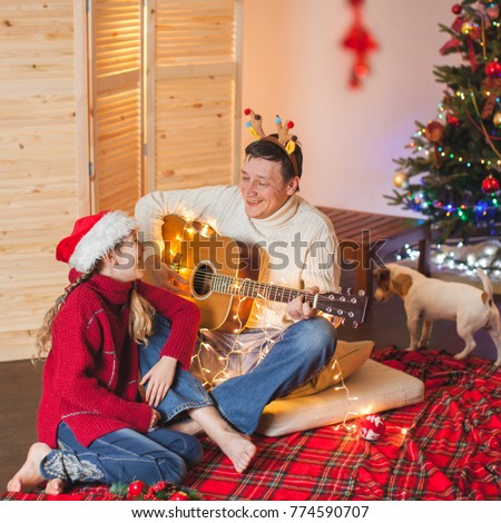 Girl with a dad playing the guitar and singing near christmas tree. Happy family near christmas tree. New Year.