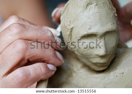 Close up to a sculptor\'s hand and female sculpture head made of clay