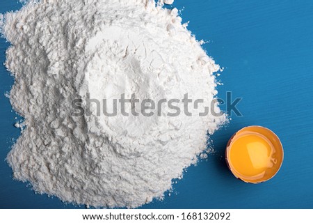 on blue kitchen table pour flour and lies next to a broken egg