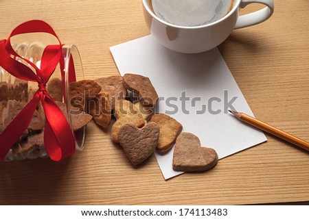 The cup of coffee on the table with a piece of paper, pencil and inverted bowl with cookie-hearts