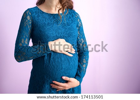 The tummy of a pregnant woman in navy-blue dress, while she is stroking it