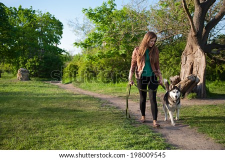 The girl is walking along the footpath with her husky dog