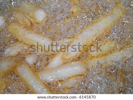 Full frame color photograph of French fries with oil bubbling all around them in a deep fryer.