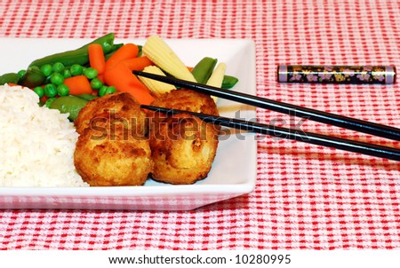 Chicken balls with rice and oriental vegetables with chop sticks leaning on the plate