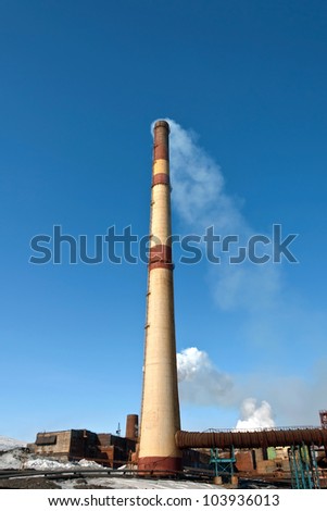 High factory chimney steel plant against the blue cloudless sky.